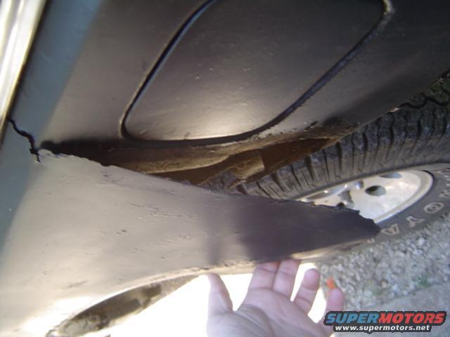 hand touching damaged metal panel near tire