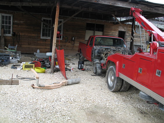 Red pickup truck with engine exposed, being towed by a red tow truck