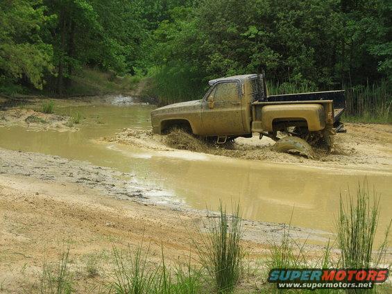 Muddy 1975 pickup truck driving through water and mud