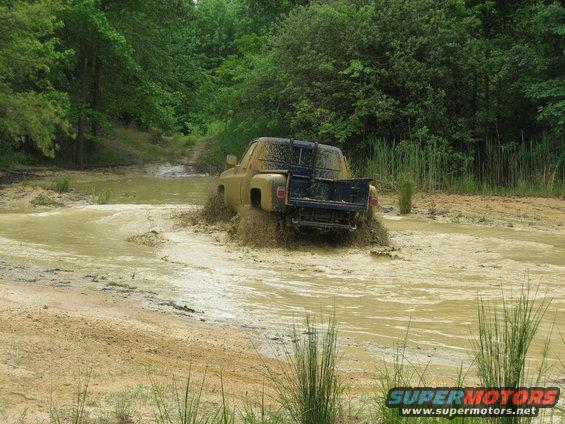 Tan pickup truck splashing through mud, rear view