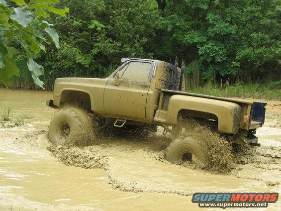 Pickup truck with large tires driving through mud and water, splashing mud everywhere