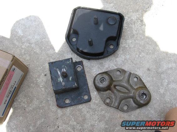 Three engine mounts and a cardboard box on a concrete surface. One mount is black rubber with metal, another is black rubber and metal, and the third is a metal bracket