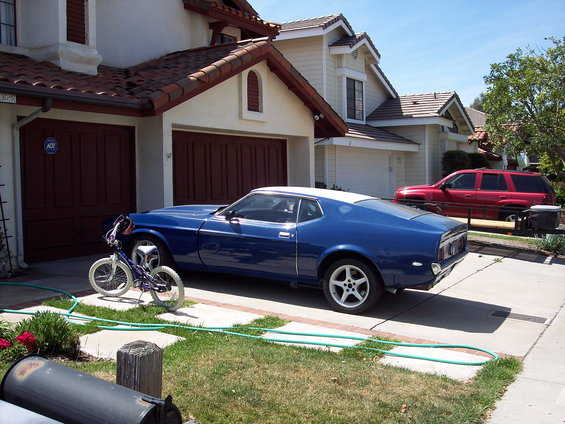 Blue coupe with white roof parked in driveway next to a red SUV. A bicycle is in front of the coupe