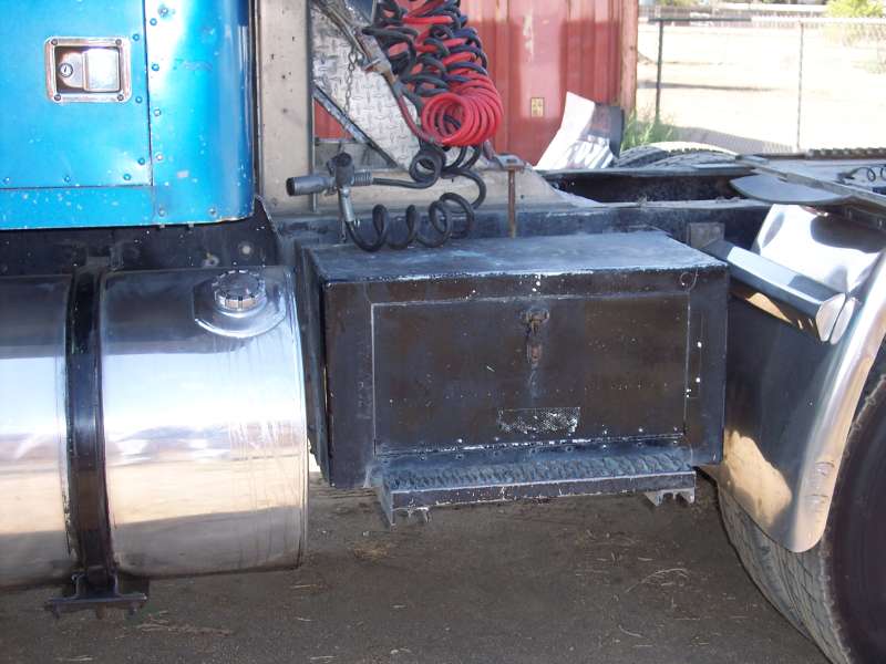 Blue truck cab corner, chrome fuel tank, and black toolbox mounted on frame