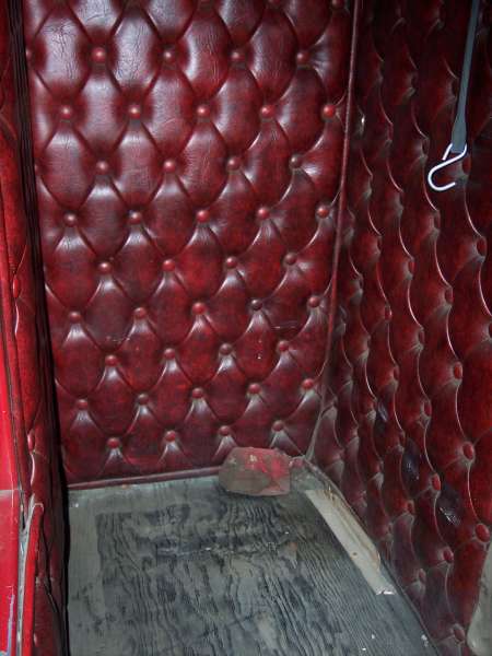 Tufted red upholstery paneling inside a vehicle, with a wooden floor and a hook on the right