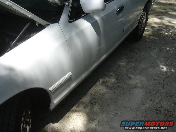 Side view of a white sedan with the hood open. Shows the front fender, door, and side trim
