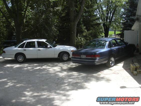 White 1997 Ford Crown Victoria and blue sedan parked on a driveway