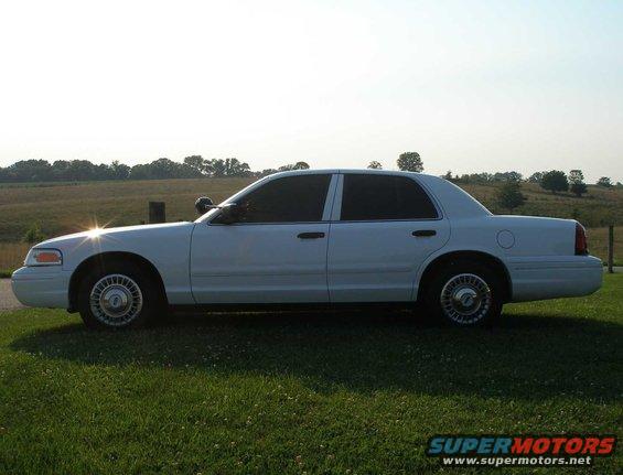 White sedan parked on grass with a field and trees in the background