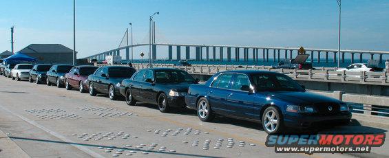 Blue Ford Crown Victoria in a line of similar cars on a bridge