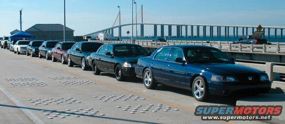 Blue Ford Crown Victoria in a line of similar cars on a bridge