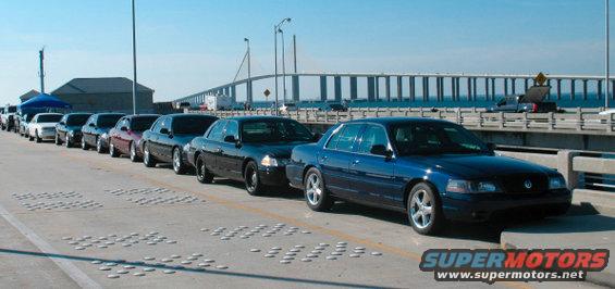 Line of Ford Crown Victoria police cars and civilian models parked on a bridge, with a blue Crown Victoria in the foreground