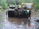 2005 Dodge 1500 - People struggle to recover a submerged off-road vehicle in a muddy waterway, with a yellow bus nearby.