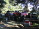 1979 Ford Bronco - Multiple modified off-road vehicles are gathered in a wooded area, with people attending to one of them.