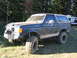 1979 Ford Bronco - A lifted Ford Bronco sits parked outdoors with trees and a camper in the background.