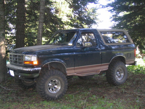 Dark green SUV with tan trim and large tires parked in a wooded area