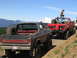1979 Ford Bronco - Several off-road vehicles, including a black Ford Bronco, are parked on a dirt road with mountains in the background.