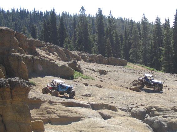 Two off-road buggies navigate a rocky, forested hillside