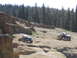 1979 Ford Bronco - Off-road vehicles traverse a challenging rocky landscape with a dense forest in the background.
