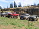 1979 Ford Bronco - Four modified off-road vehicles, including a 1979 Ford Bronco, are parked on a grassy slope with rocky terrain in the background.