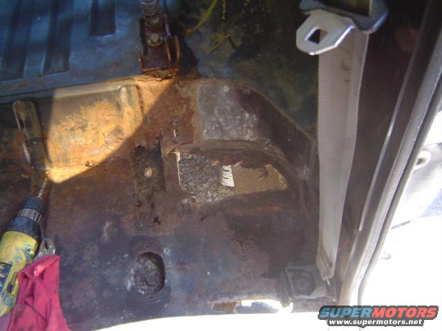 rusted out floor pan with a drill and red rag nearby