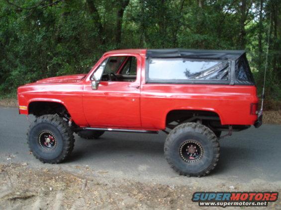 Red lifted SUV with a black soft top, large off-road tires, and side running boards