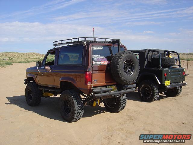 Brown 1986 Ford Bronco II rear view with spare tire on back, parked next to a green Jeep