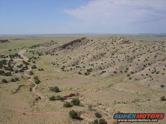 desert landscape with mesas, sparse vegetation, and a dirt road winding through the terrain