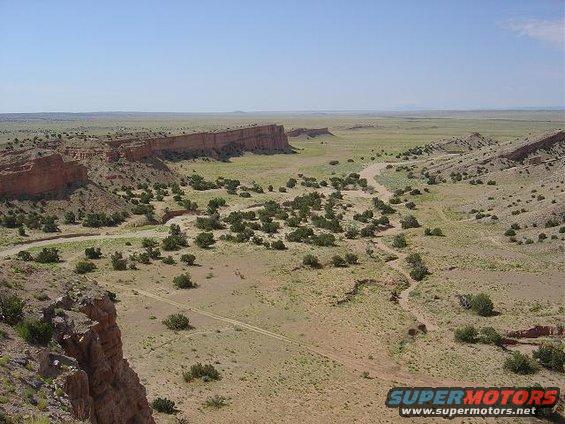 Desert landscape with mesas, sparse vegetation, and a dirt road winding through the terrain