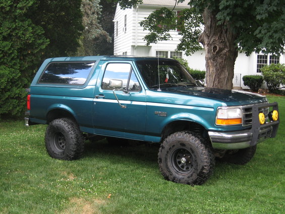 Teal 1996 Ford Bronco with lifted suspension and off-road tires parked on grass