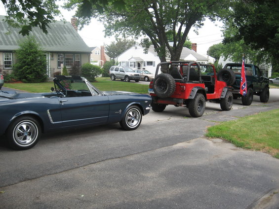 Blue convertible parked next to a red Jeep and a pickup truck flying a flag