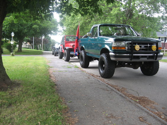Green 1996 Ford Bronco with yellow smiley face lights, followed by Jeeps