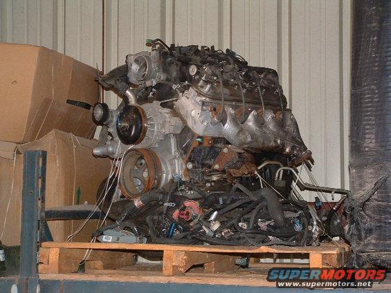 Engine assembly with wiring harness and pulleys, resting on a wooden pallet