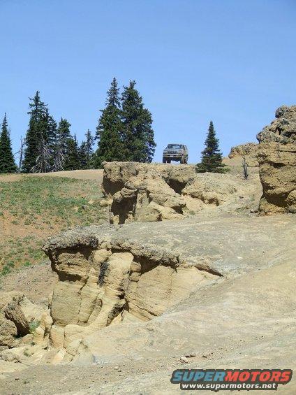 SUV parked on a rocky outcrop with trees and a clear blue sky