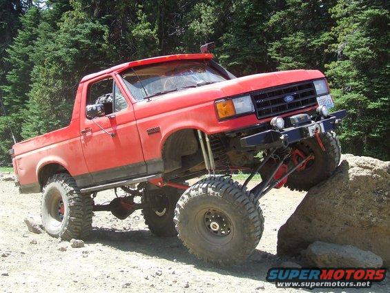 Red lifted 1987 Ford Bronco off-roading on a rock