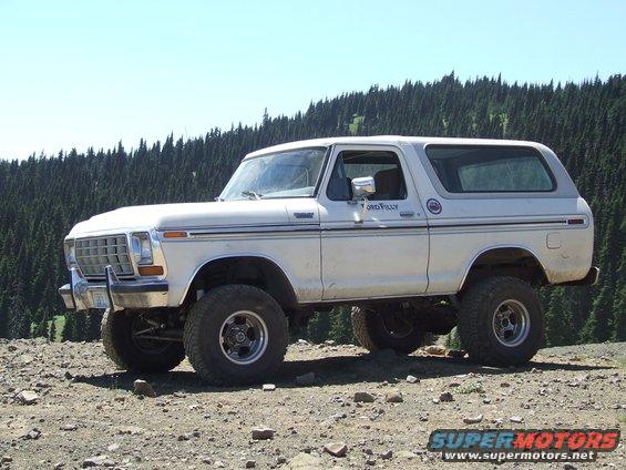 White 1978 Ford Bronco with lifted suspension and off-road tires parked on a rocky incline