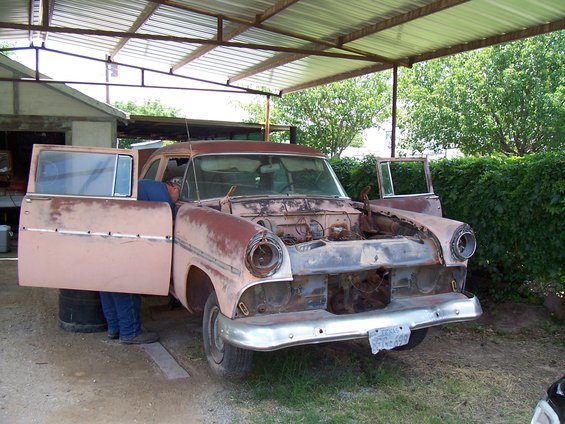 1955 Ford Customline, rusty pink, front end disassembled, doors open, under a carport