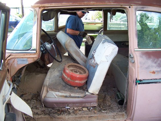 Man cleaning out interior of old car with torn seats and debris on floor