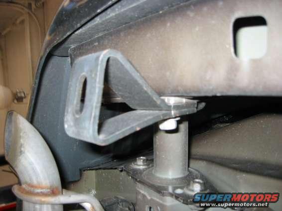 Undercarriage bracket attached to a vehicle frame, with exhaust pipe visible