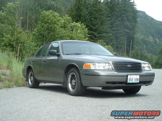 Gray 2000 Ford Crown Victoria parked on a paved road with trees and mountains in the background