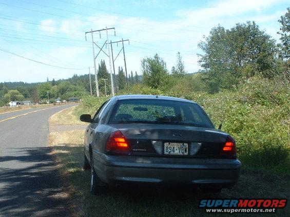 Rear view of a dark 2000 Ford Crown Victoria parked on a grassy shoulder