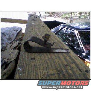 metal clamp bolted to a wooden beam, with part of a car visible in the background