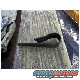 Black metal clip with a curved end rests on a weathered wooden surface with white debris