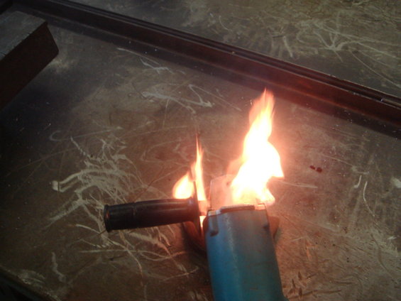 Angle grinder with flames coming out of it, sitting on a scratched surface