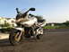 2003 Suzuki Bandit S - A silver 2003 Suzuki Bandit S motorcycle is parked on an asphalt surface under a clear blue sky.