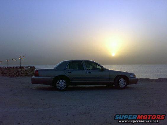 sedan parked on beach with sun setting over water