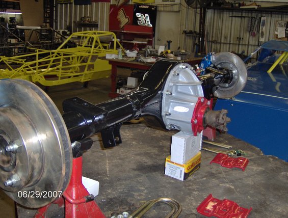 rear axle assembly on jack stands, disc brakes installed, shop background with car frames