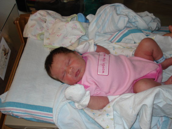 Newborn baby in pink onesie with 'worth the wait' tag, sleeping on a blanket