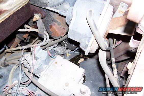 Close-up of engine bay with various wires, hoses, and electrical components. Some rust is visible on metal parts