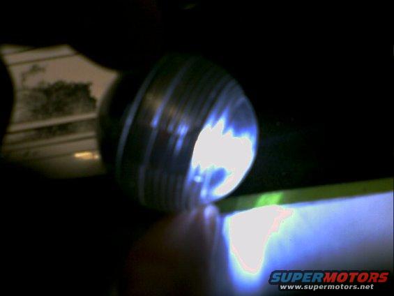 Headlight assembly with ribbed casing and bright blue light, partially obscured by a hand