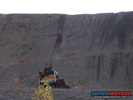 ATV driving up a steep coal pile with a rusty metal structure at the bottom